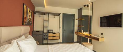 A modern hotel room with a large bed, a wardrobe, a desk with a chair, a mirror, and a TV mounted on the wall.