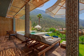 Un área de descanso al aire libre con muebles de madera, una piscina y vistas a un paisaje montañoso.