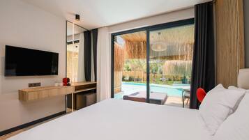 A hotel room with a large bed, a TV mounted on the wall, a wooden desk, and a view of a swimming pool through large glass doors.
