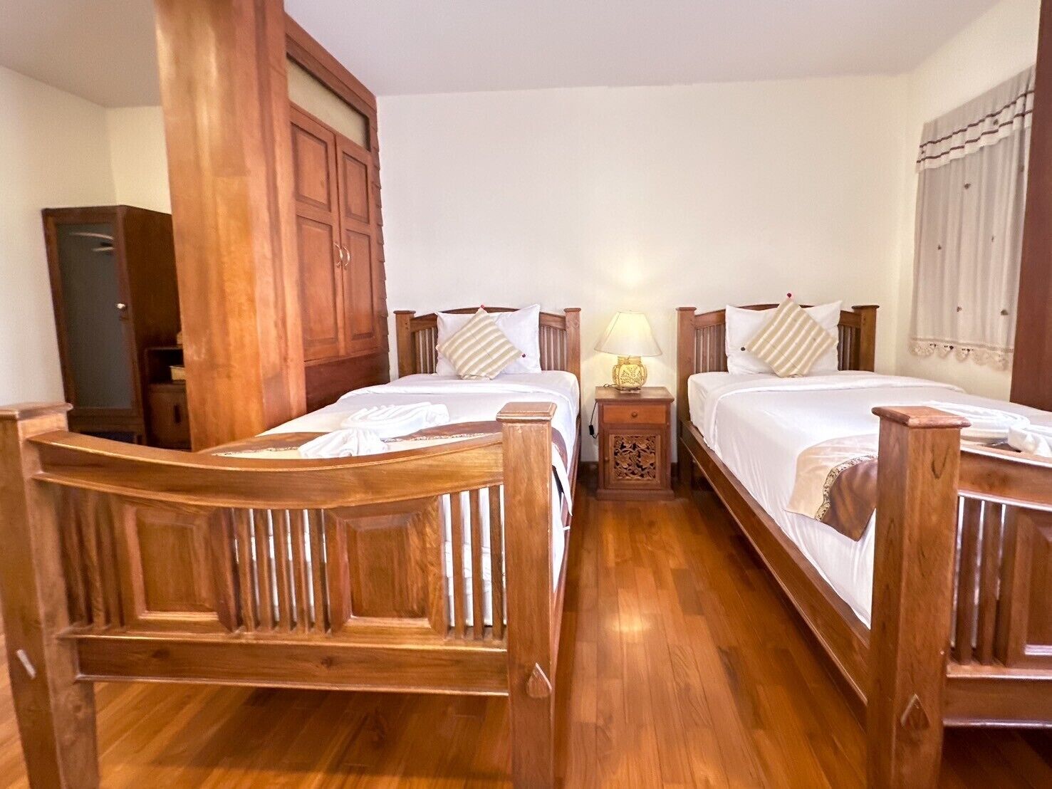 Una habitación con dos camas de madera, una mesita de noche con una lámpara, un armario de madera y piso de madera.