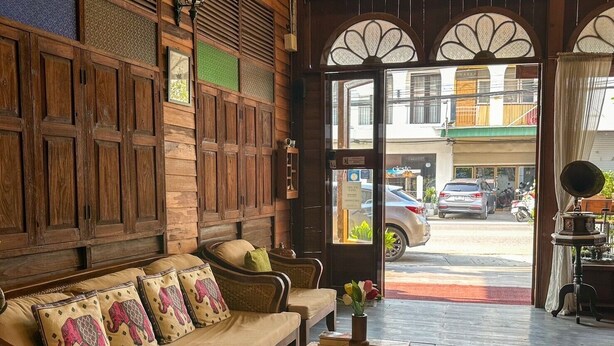 A cozy room with a wooden sofa, a wicker coffee table, and a view of the street outside. - Rustic River Boutique (Chiang Mai)