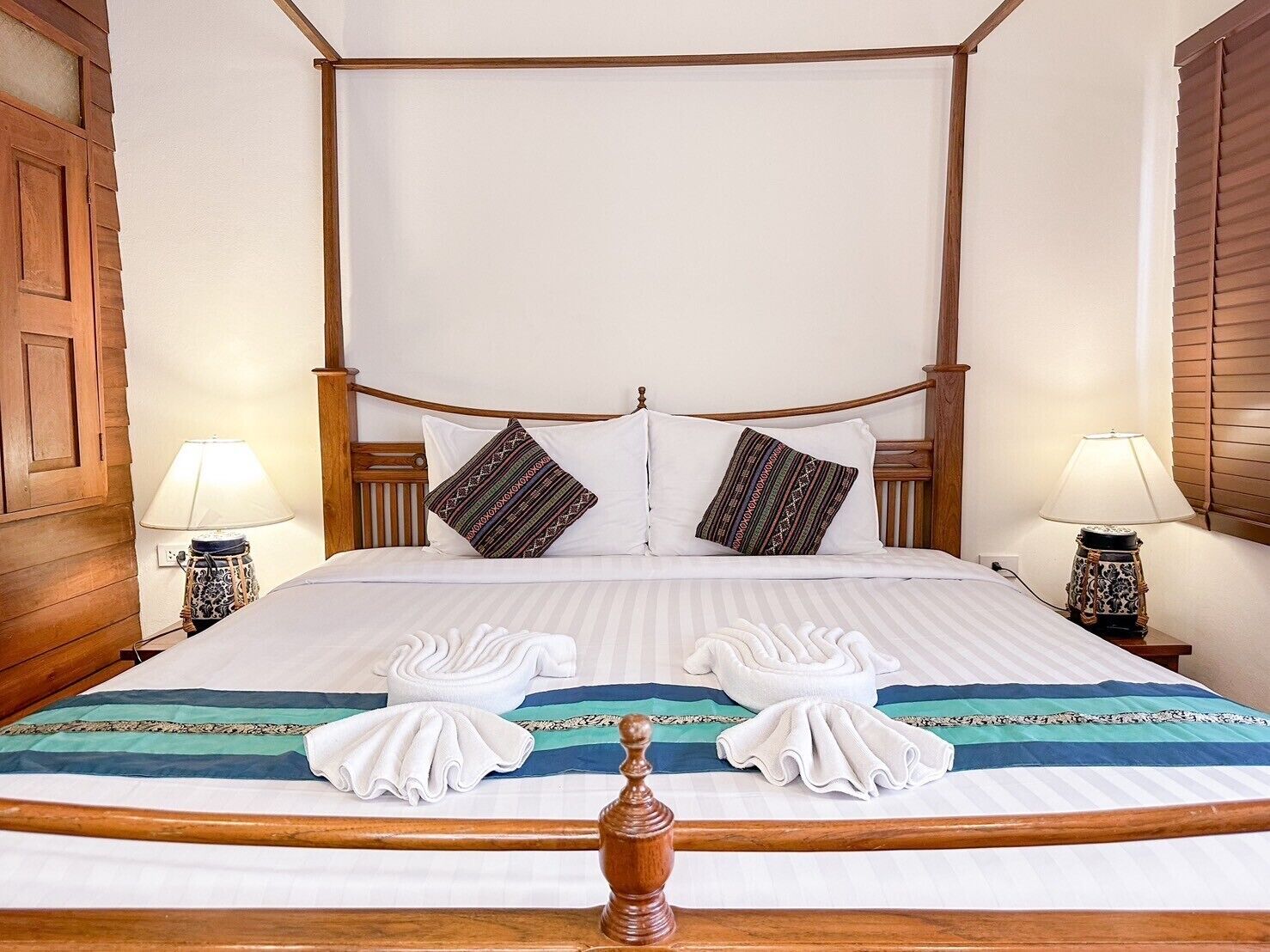 Ein Bett mit Baldachin, mit Holzrahmen, weißen Leinentüchern, zwei gemusterten Kissen und zwei auf dem Bett gefalteten Handtüchern.