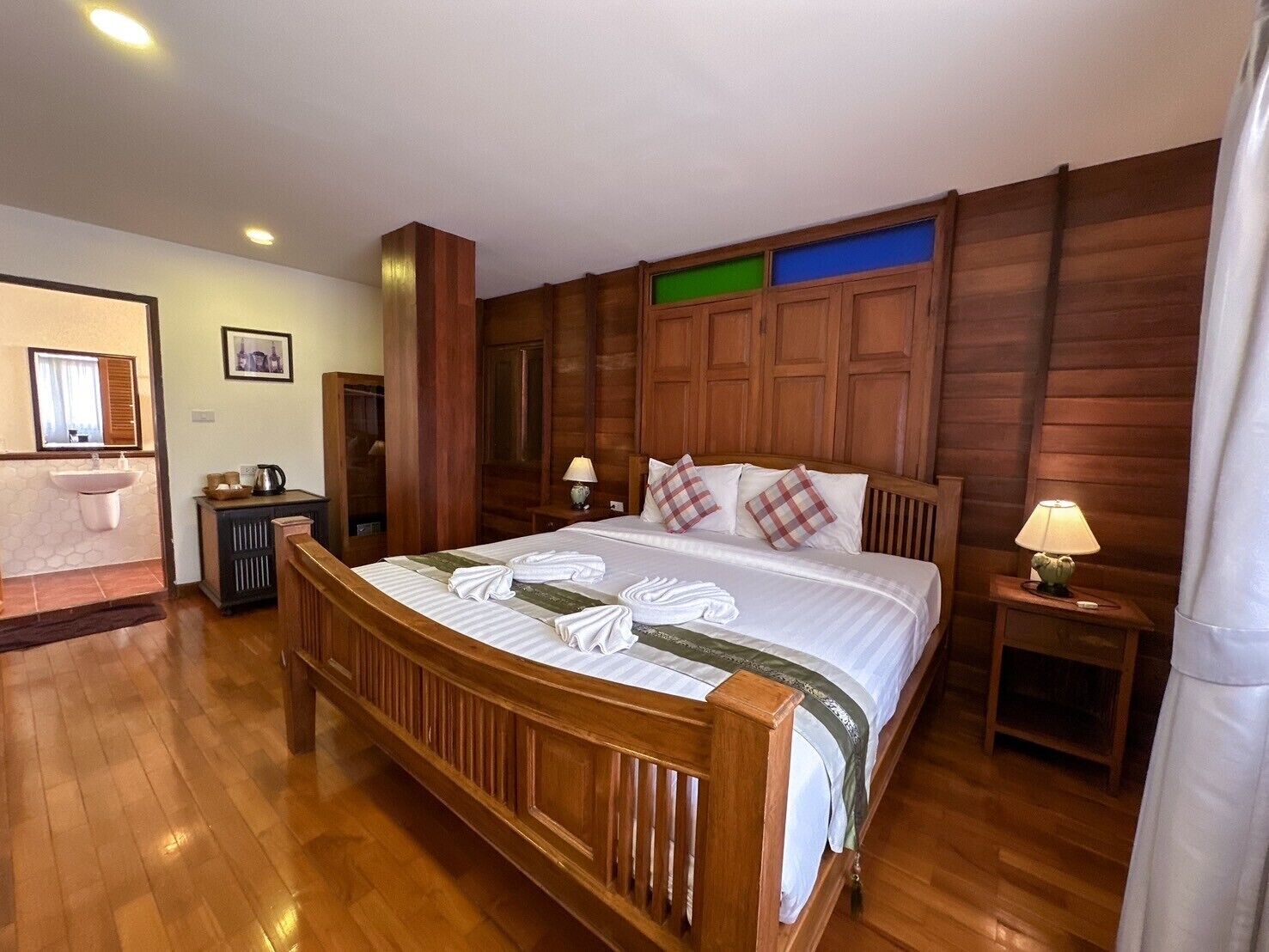 A wooden-framed bed with white linens and plaid pillows, a bedside table with a lamp, and a wooden wardrobe.