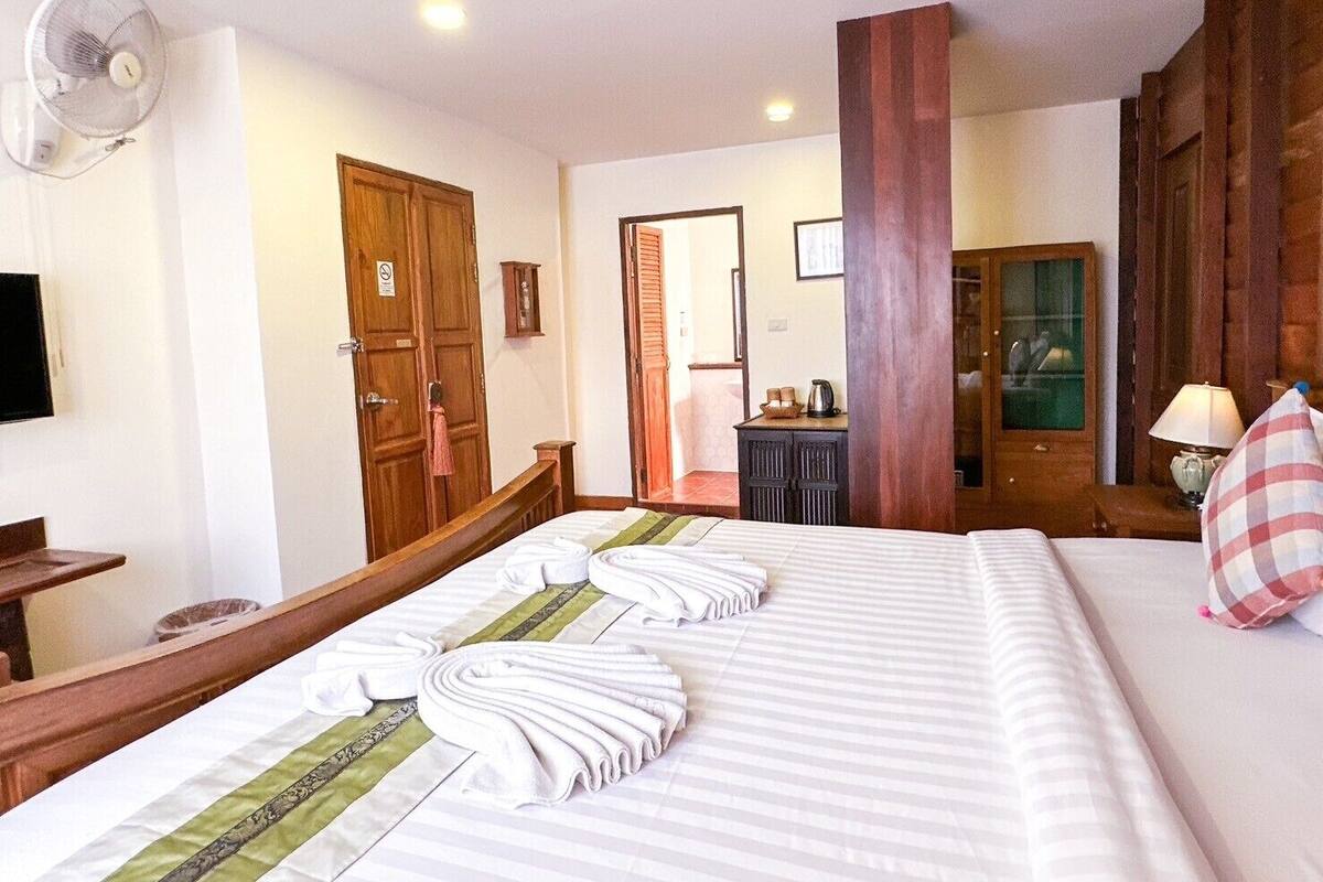 A hotel room with a large bed, a wooden headboard, a desk with a chair, a television, and a wardrobe.