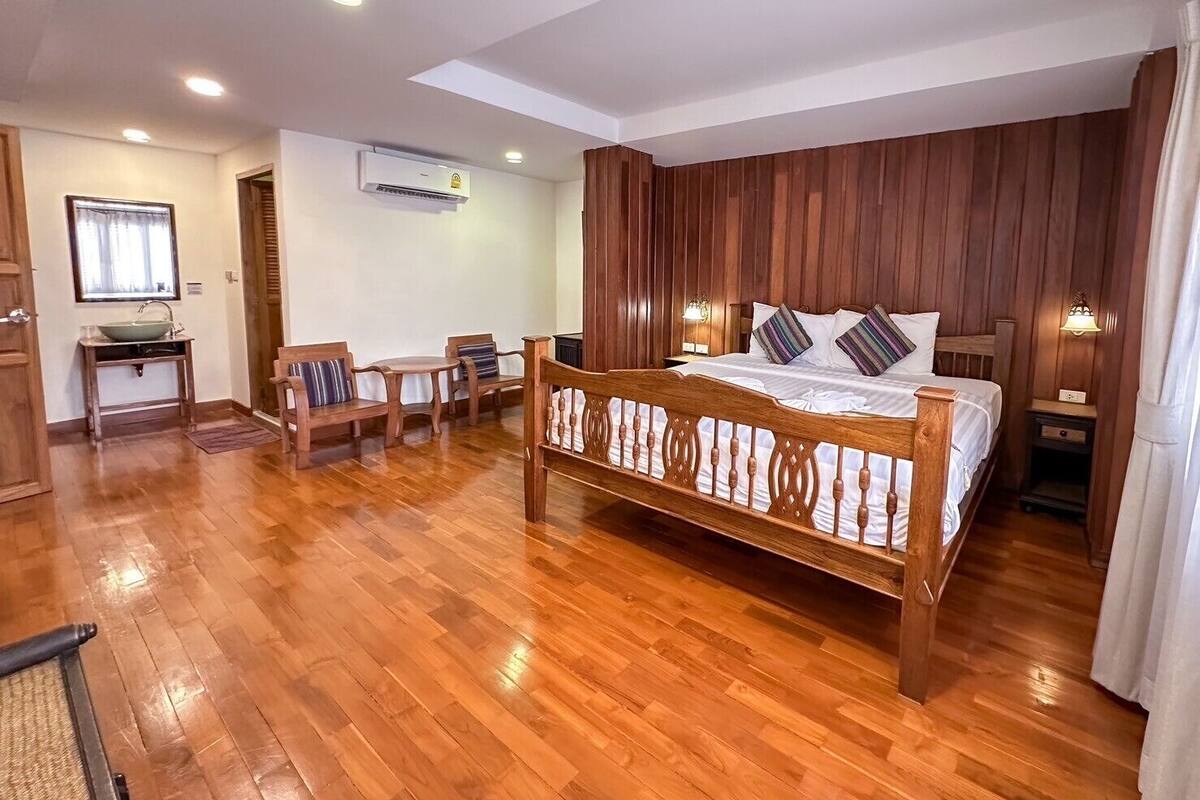 A bedroom with a wooden bed, a desk, chairs, and a window with curtains.