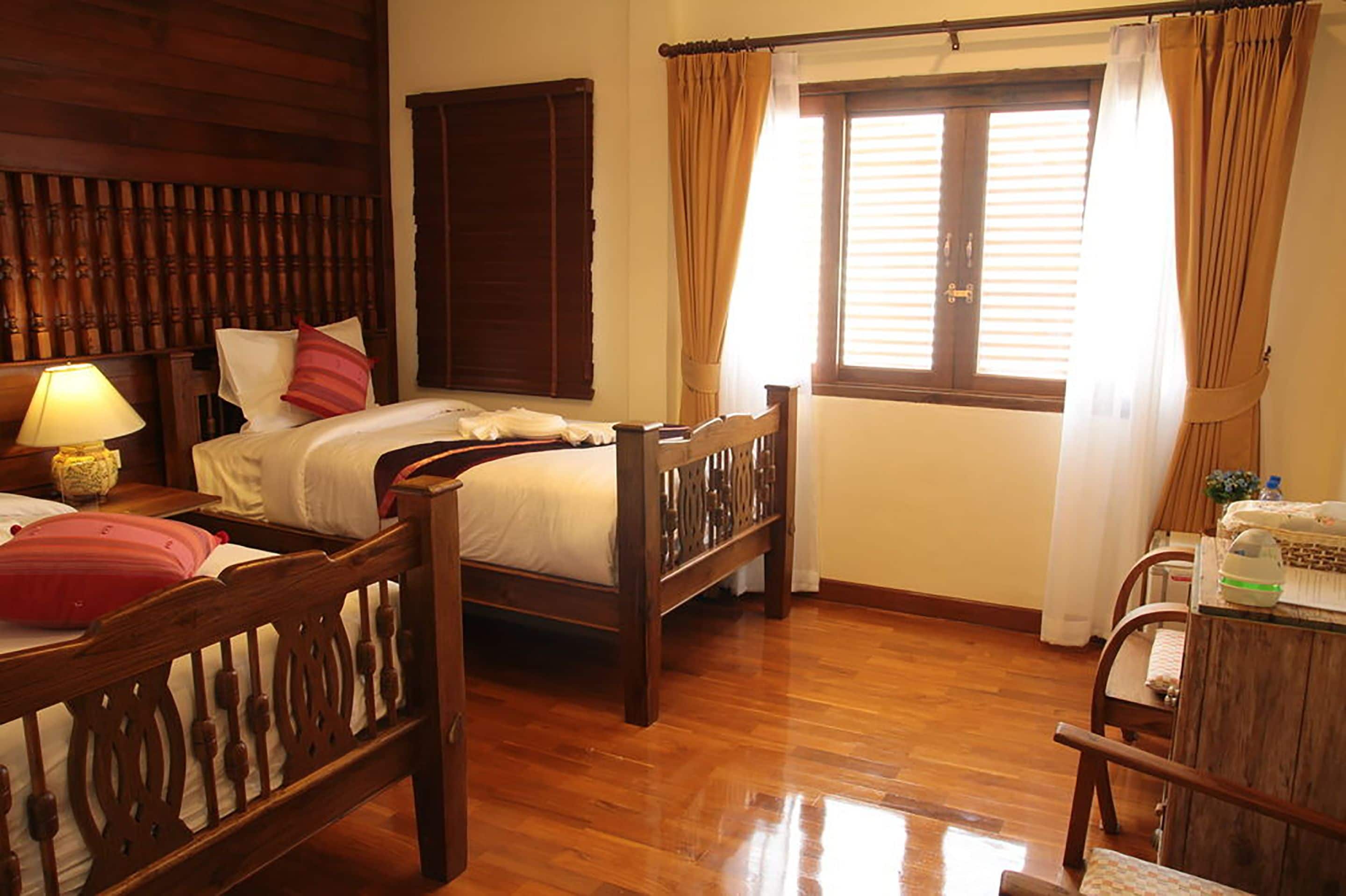 A traditional wooden bedroom with a bed, two nightstands, a lamp, and a window with curtains.