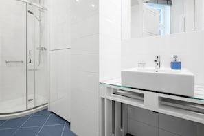 A modern bathroom with a glass shower enclosure, a white sink with a glass countertop, and a large mirror above the sink.