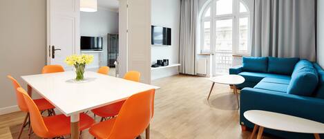 Una sala de estar moderna con una mesa de comedor blanca, sillas naranjas, un sofá azul y una pequeña mesita auxiliar blanca.