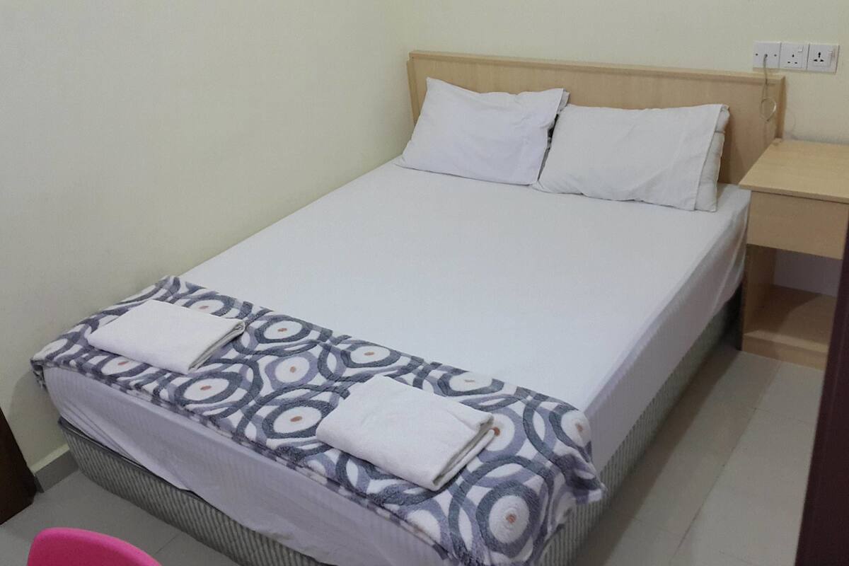 A single bed with a patterned bedspread, two pillows, and a wooden headboard.