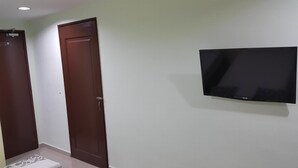 A room with a closed wooden door, a wall-mounted flat-screen TV, and a small rug on the floor. - First and New Star Hotel (Kuala Lumpur)