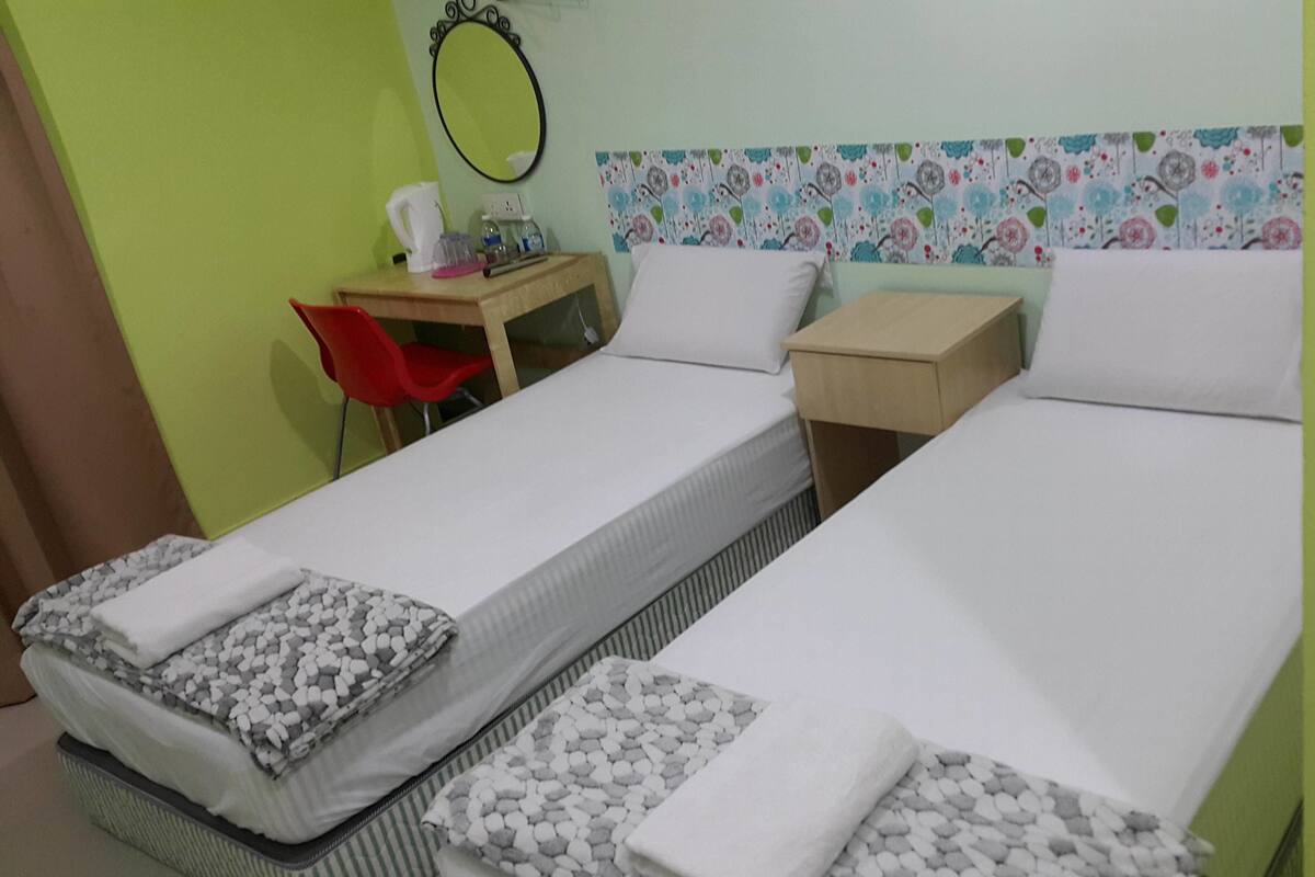 A room with two single beds, a desk with a chair, a mirror, and a small table with a kettle and cups.