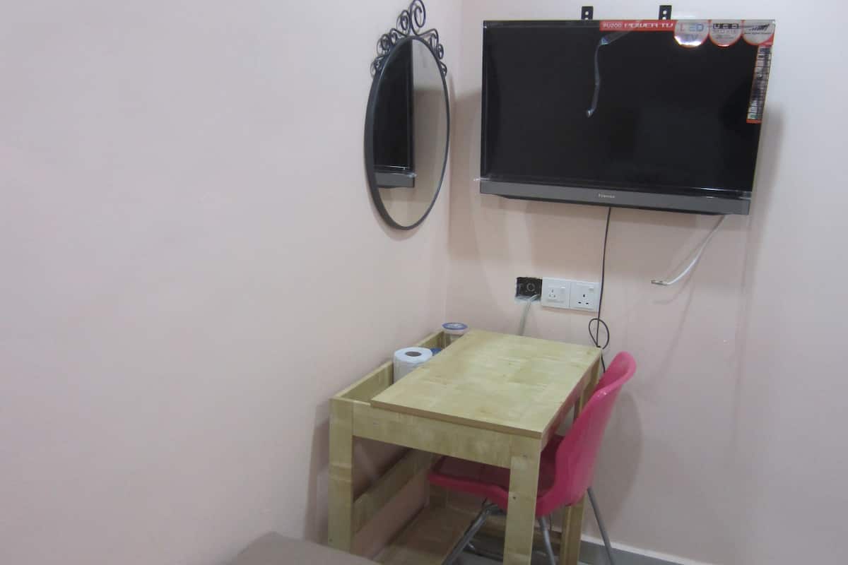A small room with a bed, a desk with a chair, a TV mounted on the wall, and a mirror.