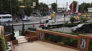 Un espacio público al aire libre con una escalera que sube, una zona pavimentada con un logotipo y vistas de una calle concurrida, vehículos y edificios.