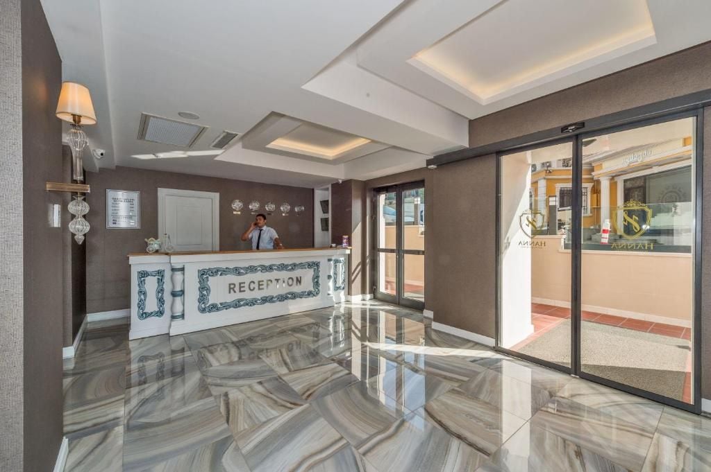 Zona de recepción con suelo de mármol, mostrador de recepción y vista a un restaurante a través de puertas de vidrio.