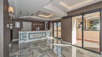 Zona de recepción con suelo de mármol, mostrador de recepción y vista a un restaurante a través de puertas de vidrio.