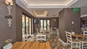 Un restaurant avec des tables en bois et des chaises blanches, un téléviseur fixé au mur et un sol à motifs.