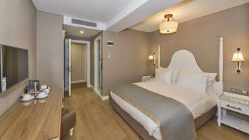 A hotel room with a bed, bedside tables, a desk with a chair, a TV, and a door leading to another room.