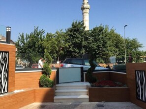 A building entrance with a staircase leading up to a gated area, a tall tower in the background, and a street with cars and people. - Hanna Hotel (Istanbul)
