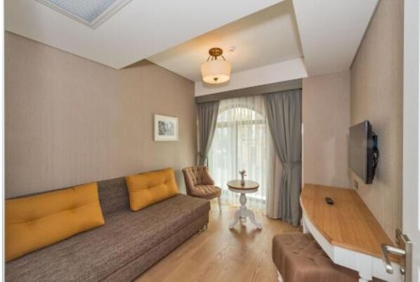 A modern living room with a sofa, armchair, small table, and a TV mounted on the wall. - Hanna Hotel (Istanbul)