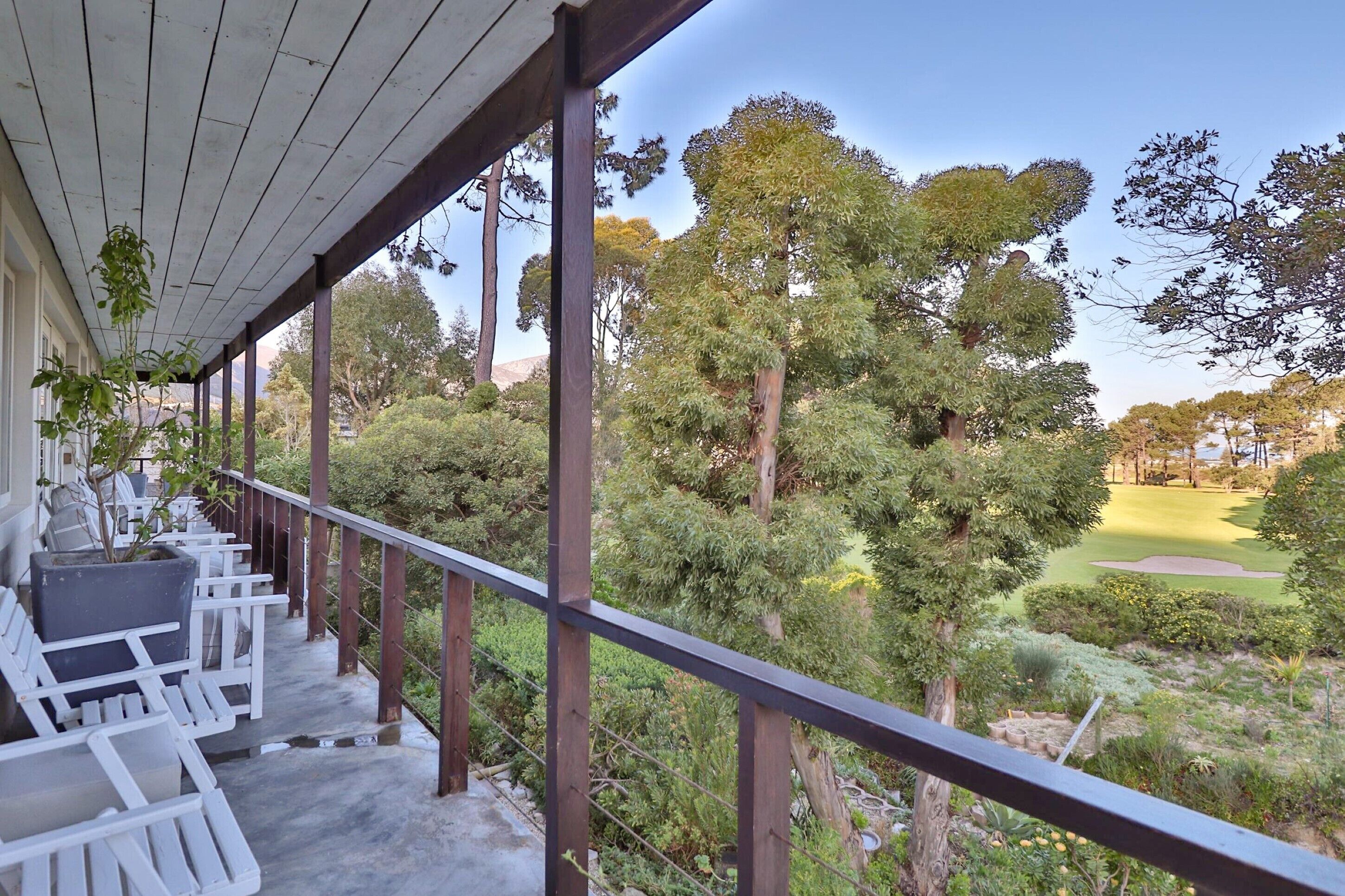 A covered balcony with white chairs and a view of a golf course.
