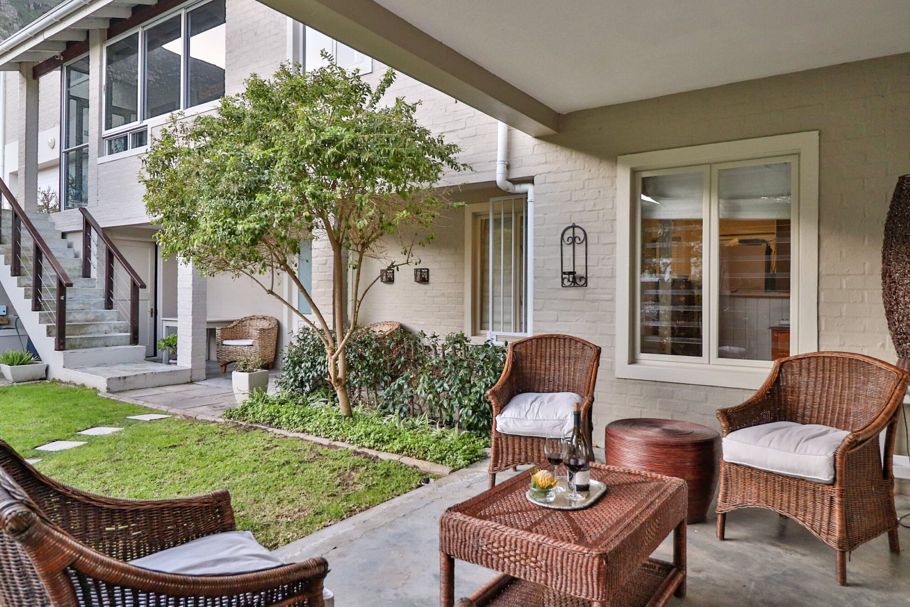 A patio area with wicker furniture, a small tree, and a staircase leading to the building.