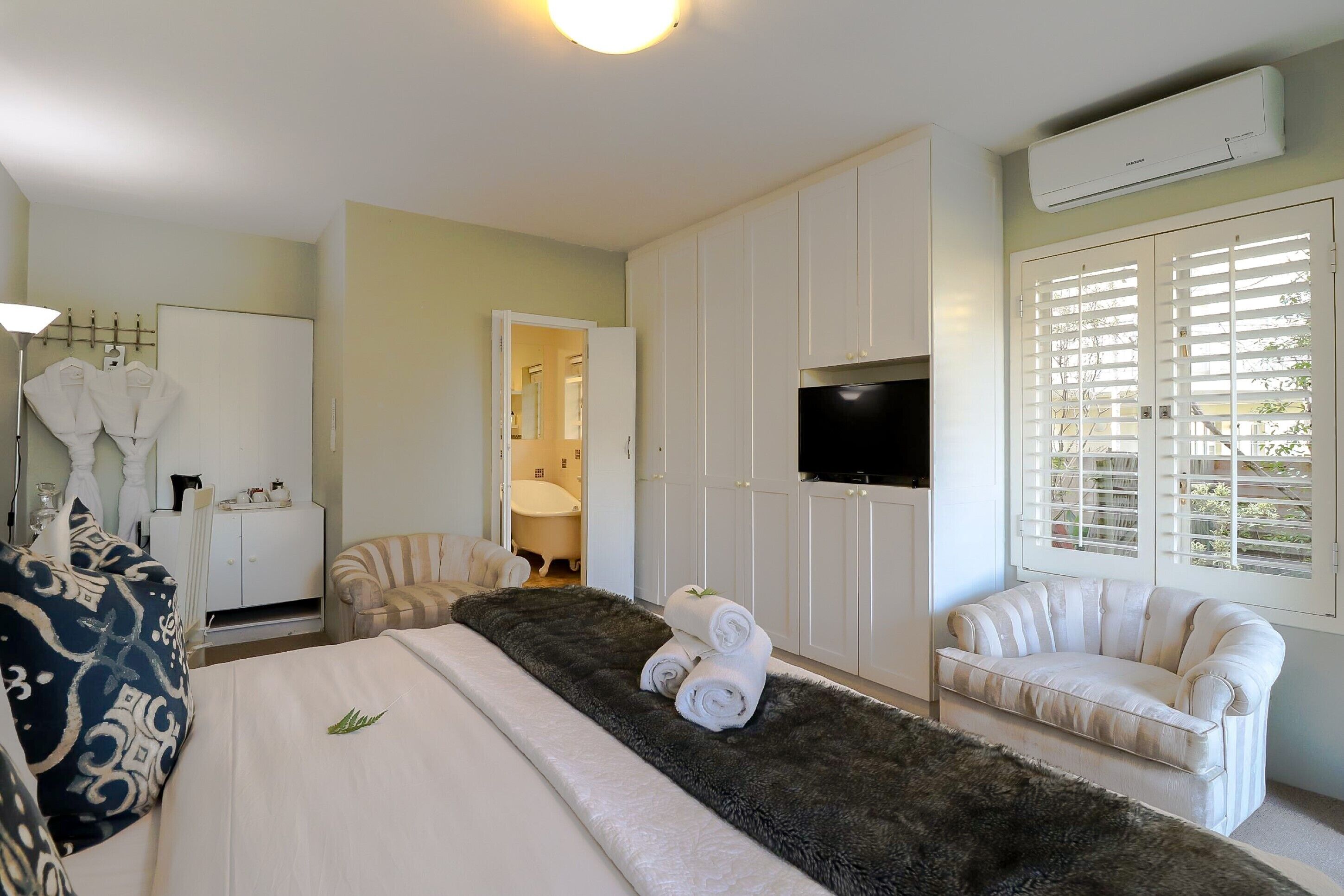 A hotel room with a bed, a sofa, a TV, and a window with blinds.