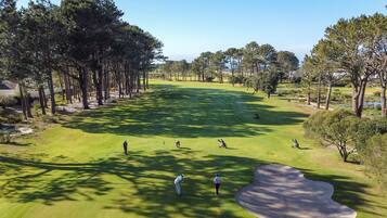 Campo de golf con un bunker de arena, árboles y cielo despejado.