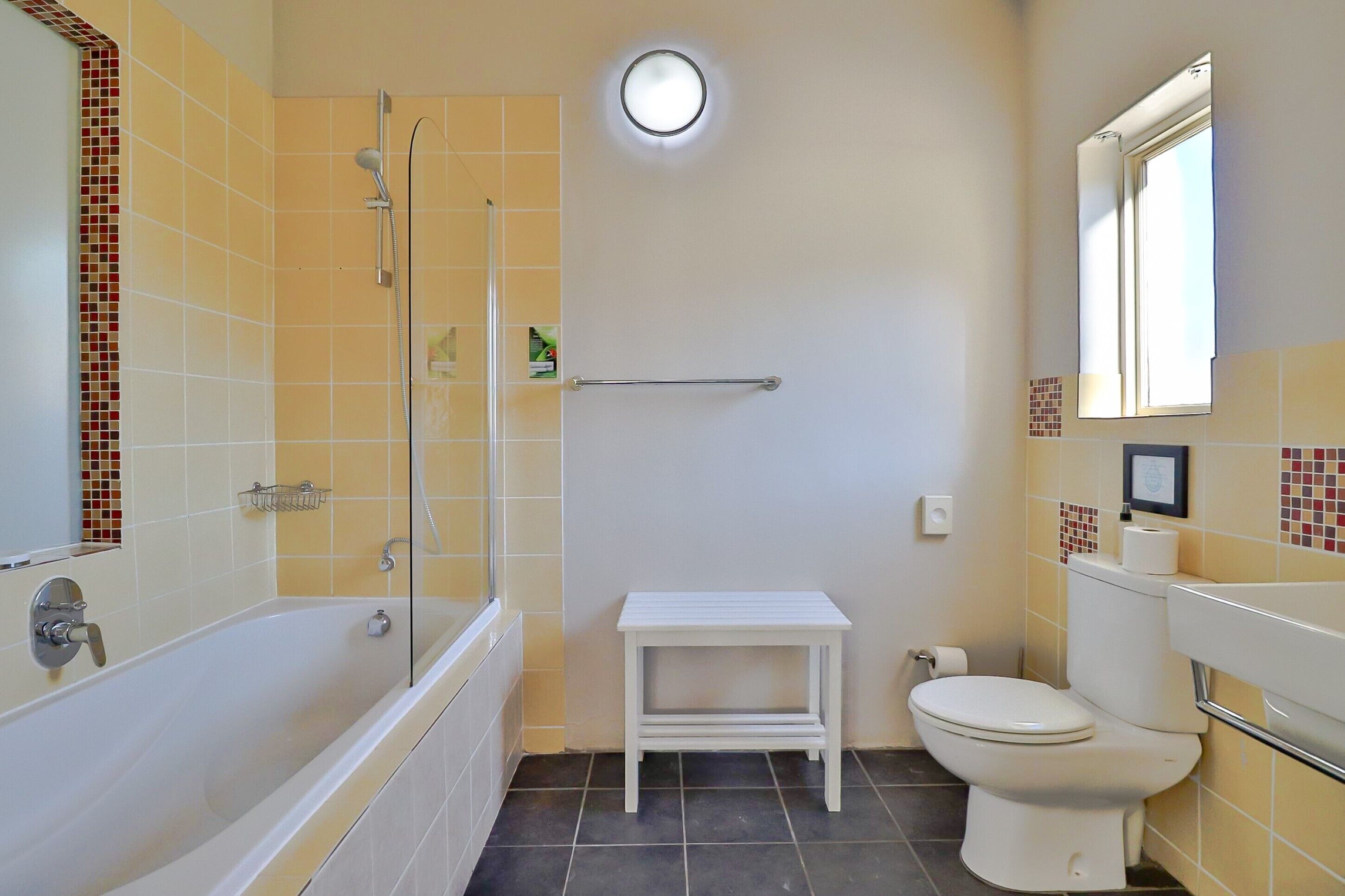 A bathroom with a bathtub, toilet, and a small white table.