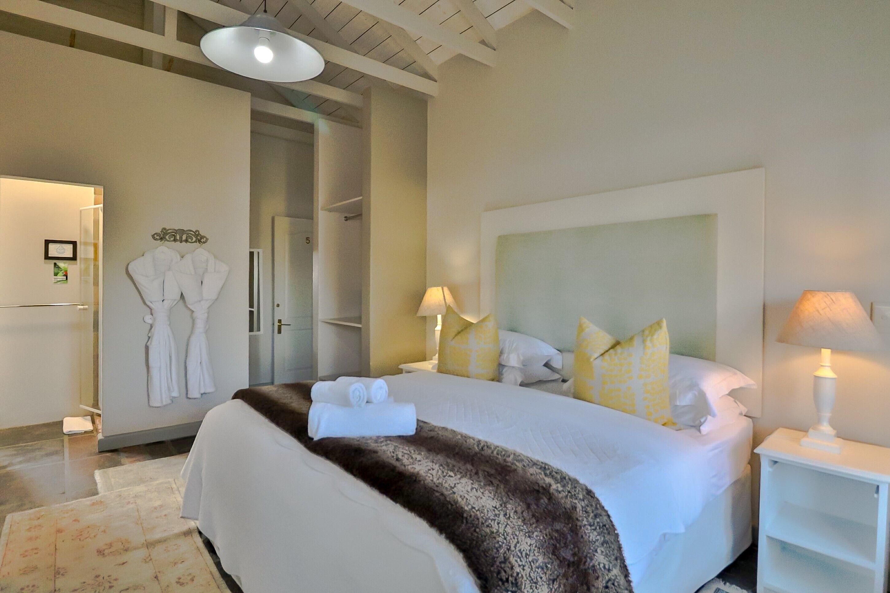 A hotel room with a large bed, two bedside lamps, a headboard, and a wardrobe with hanging robes.