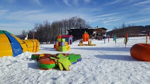 A snowy outdoor area with colorful play structures, a tent, and a building in the background. - Residence Cimone (Riolunato)