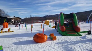 An outdoor snowy area with inflatable play structures and a building in the background. - Residence Cimone (Riolunato)