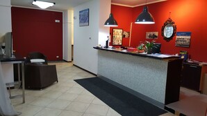 A reception area with a red wall, a reception desk, a chair, and a desk lamp. - Residence Cimone (Riolunato)
