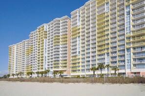 A high-rise hotel with multiple balconies, located near a beach.
