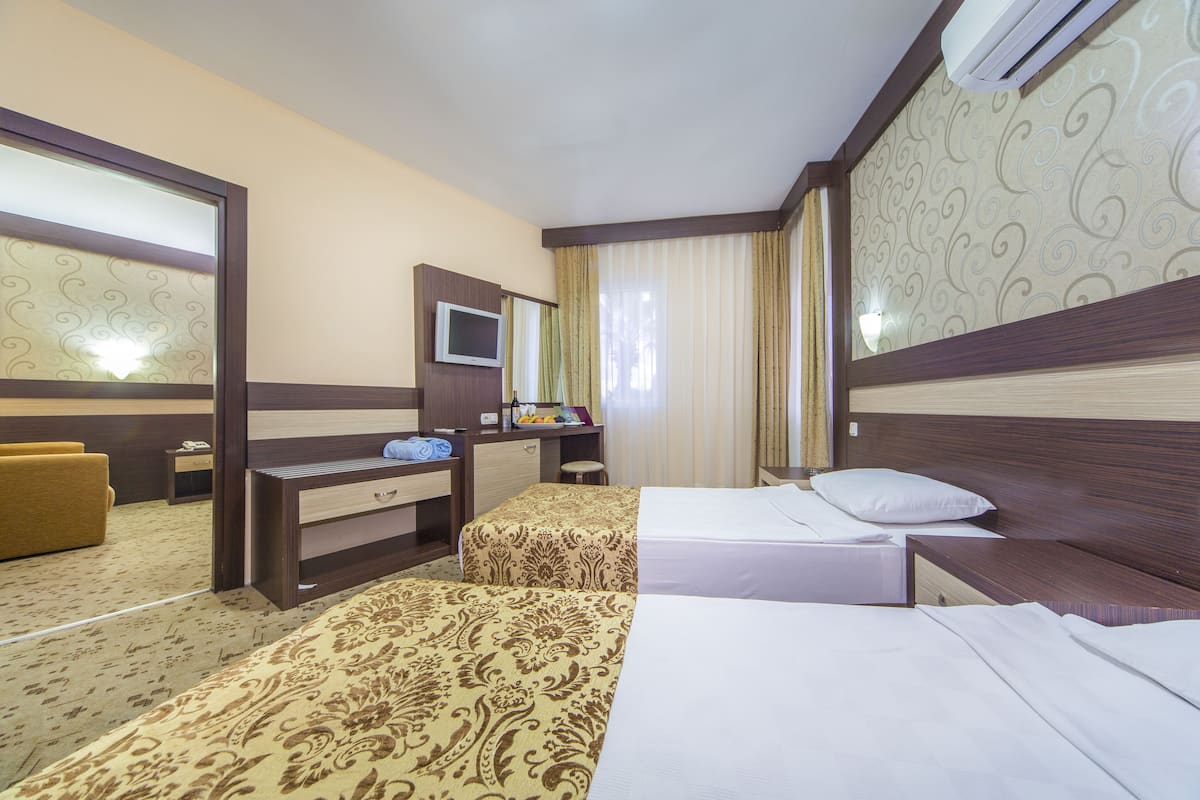 A hotel room with two beds, a desk with a TV, a small table, and a chair.