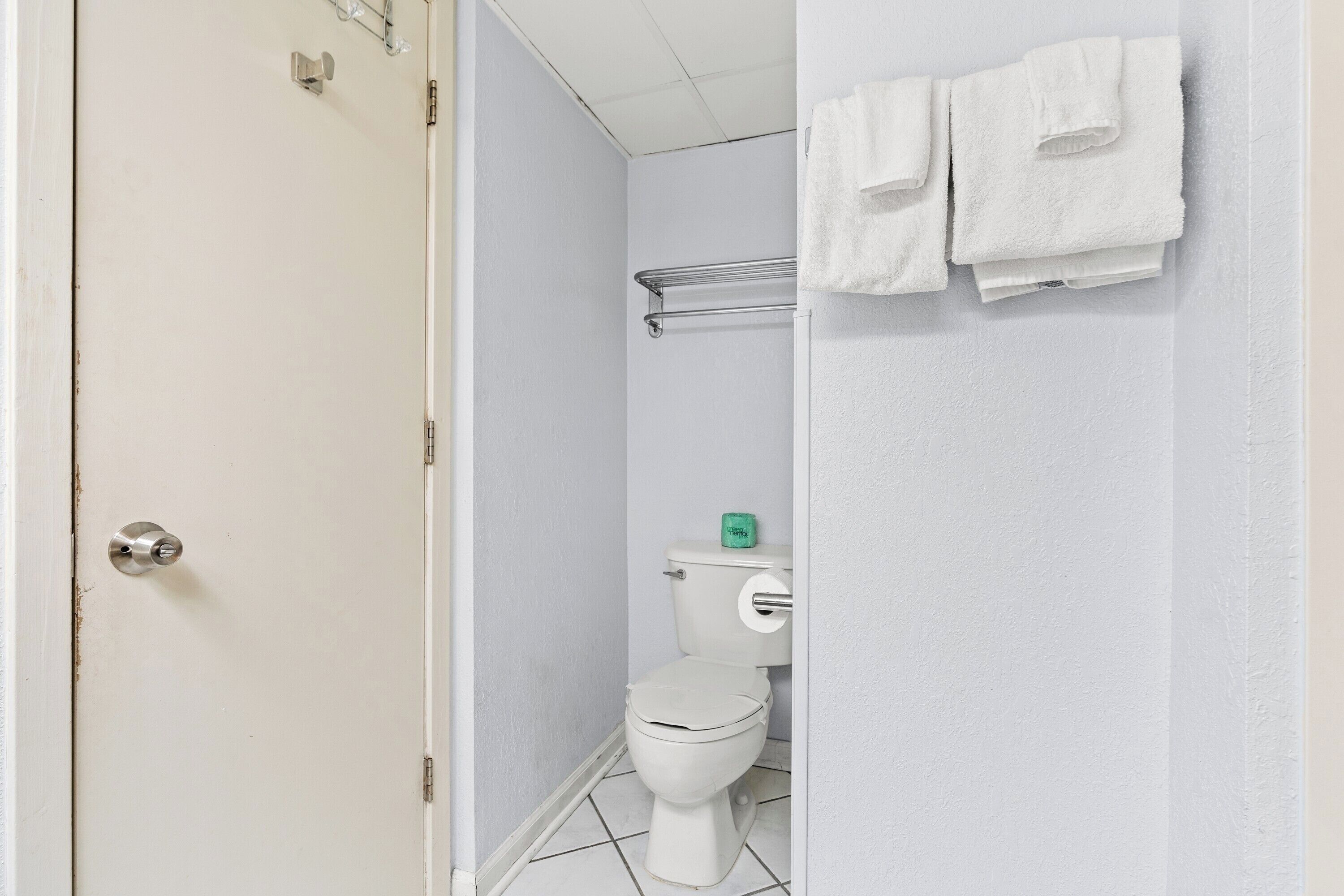 Un baño con inodoro, toallero y toallas, y una puerta.