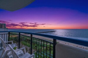 A balcony with a view of the ocean at sunset, a pier, and a row of beach chairs. - Boardwalk Beach Resort by Elliott Beach Rentals (Myrtle Beach)