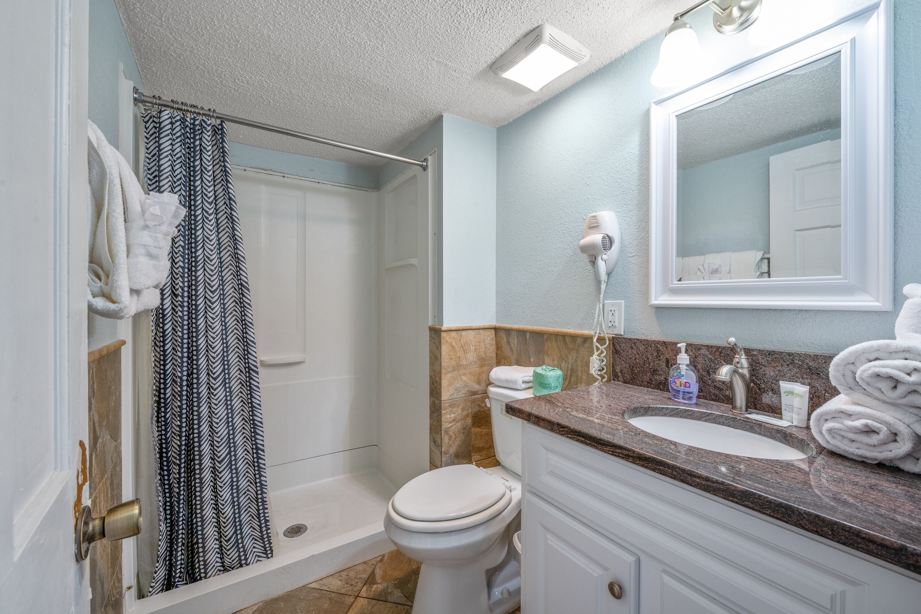 A bathroom with a shower, toilet, sink, and a mirror.