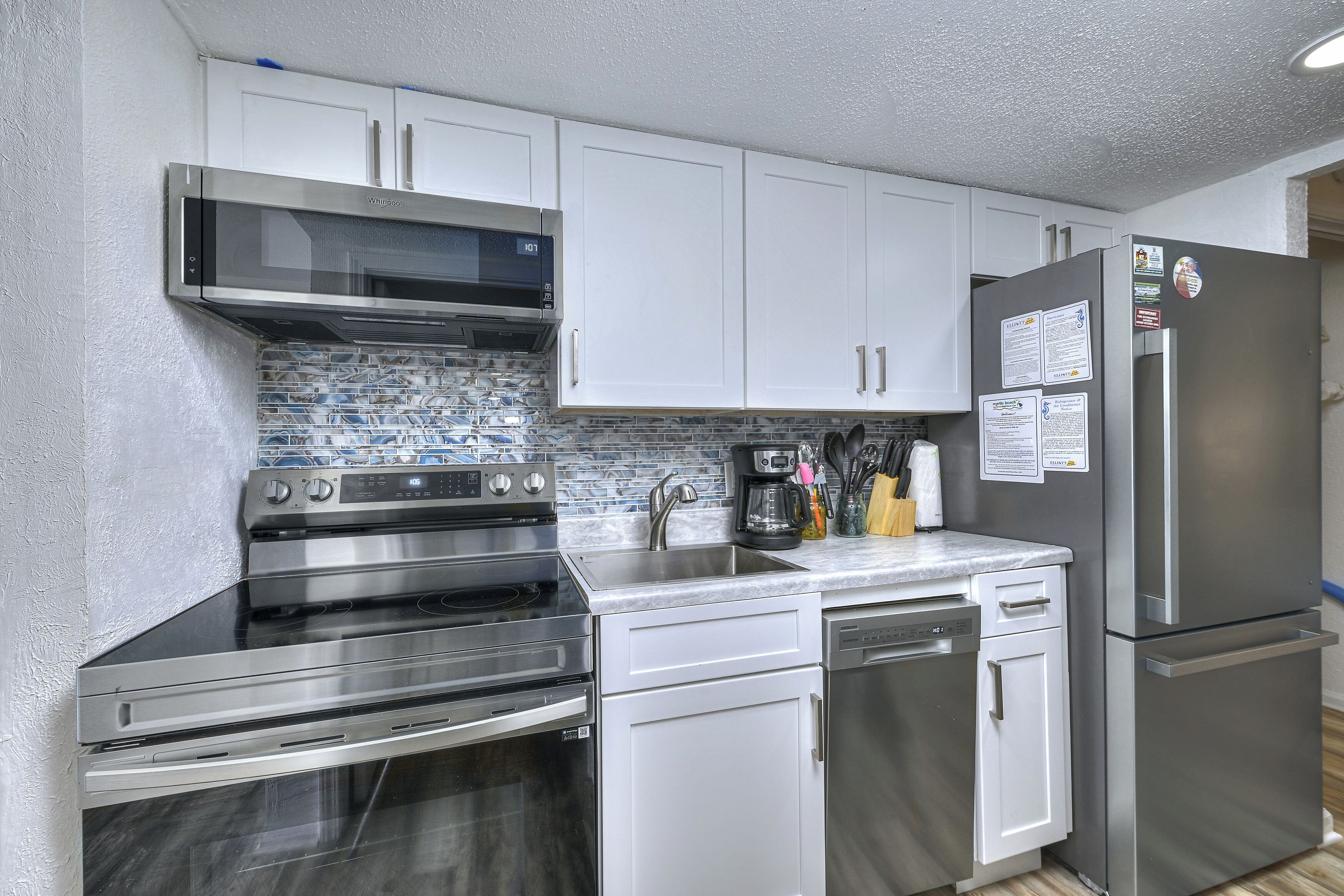 Una cocina moderna con electrodomésticos de acero inoxidable, armarios blancos y salpicadero de azulejos.