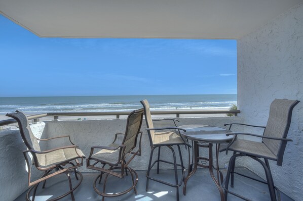 A balcony with wicker chairs and a table overlooking the ocean.