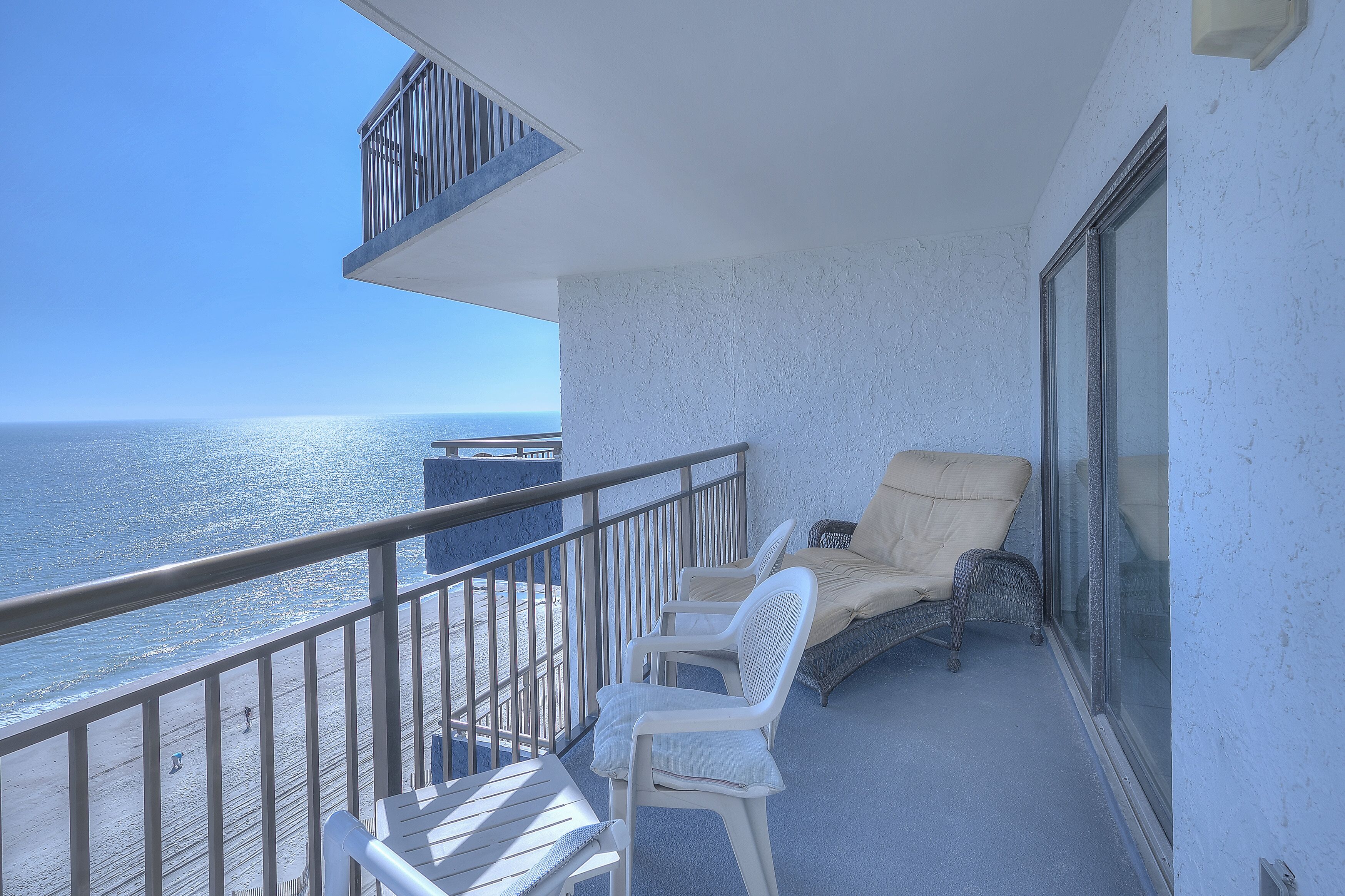 A balcony with a view of the ocean, white chairs, and a table.