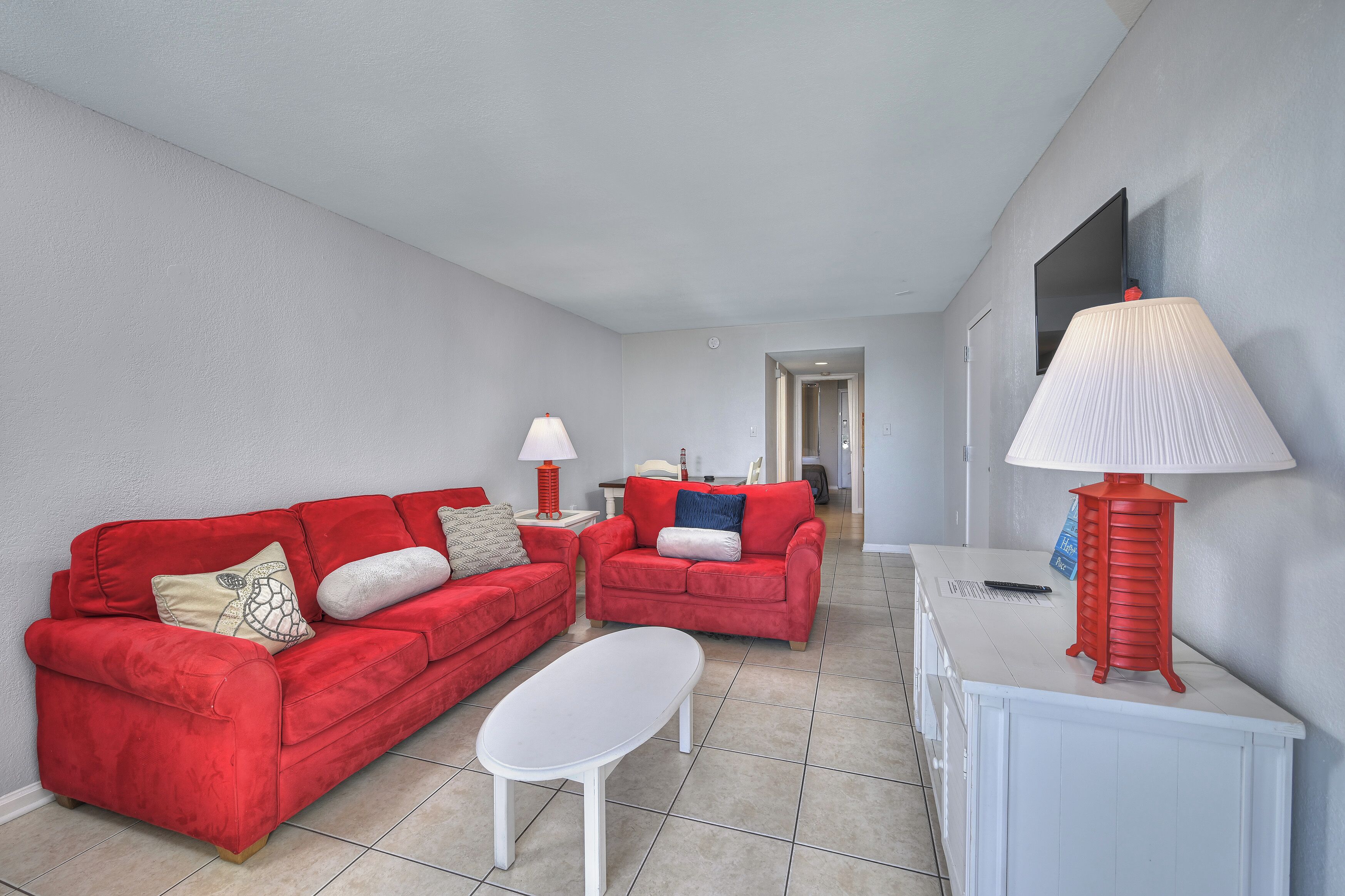 A living room with two red sofas, a white coffee table, and a red lamp on a white console table.