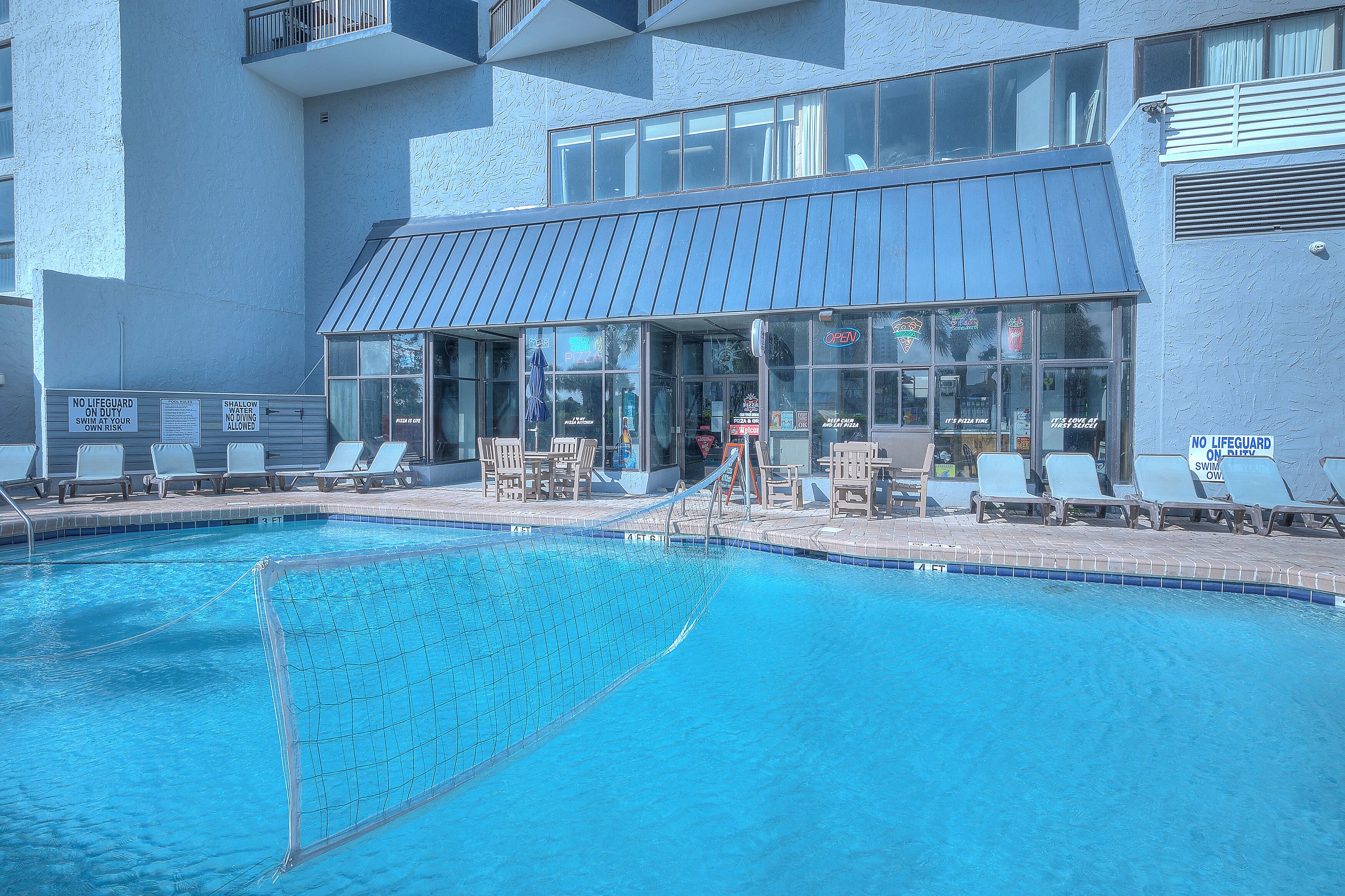 A swimming pool with lounge chairs and a building with large windows.