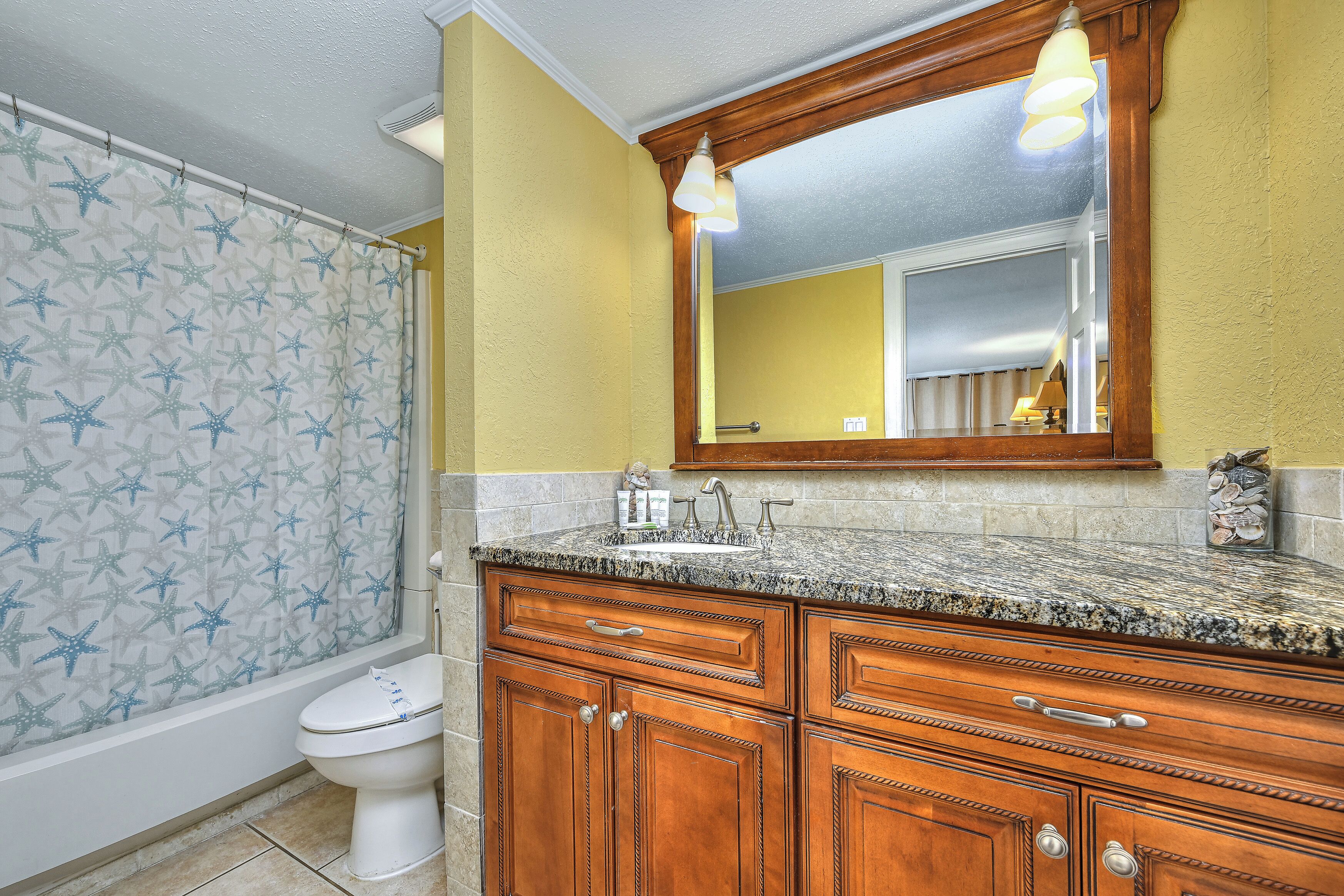 A bathroom with a shower curtain, a toilet, wooden cabinets, and a mirror.