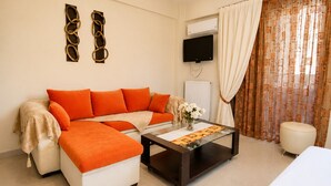 Una sala de estar moderna con sofá, reposapiés, mesa de centro, televisor, equipo de aire acondicionado y cortinas.