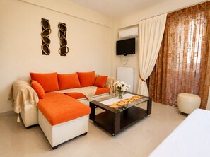 Ein modernes Wohnzimmer mit Sofa, Hocker, Couchtisch, Fernseher, Klimaanlage und Vorhängen.