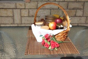 Una cesta de mimbre con frutas, un tarro y un ramo de flores sobre una mesa de vidrio.
