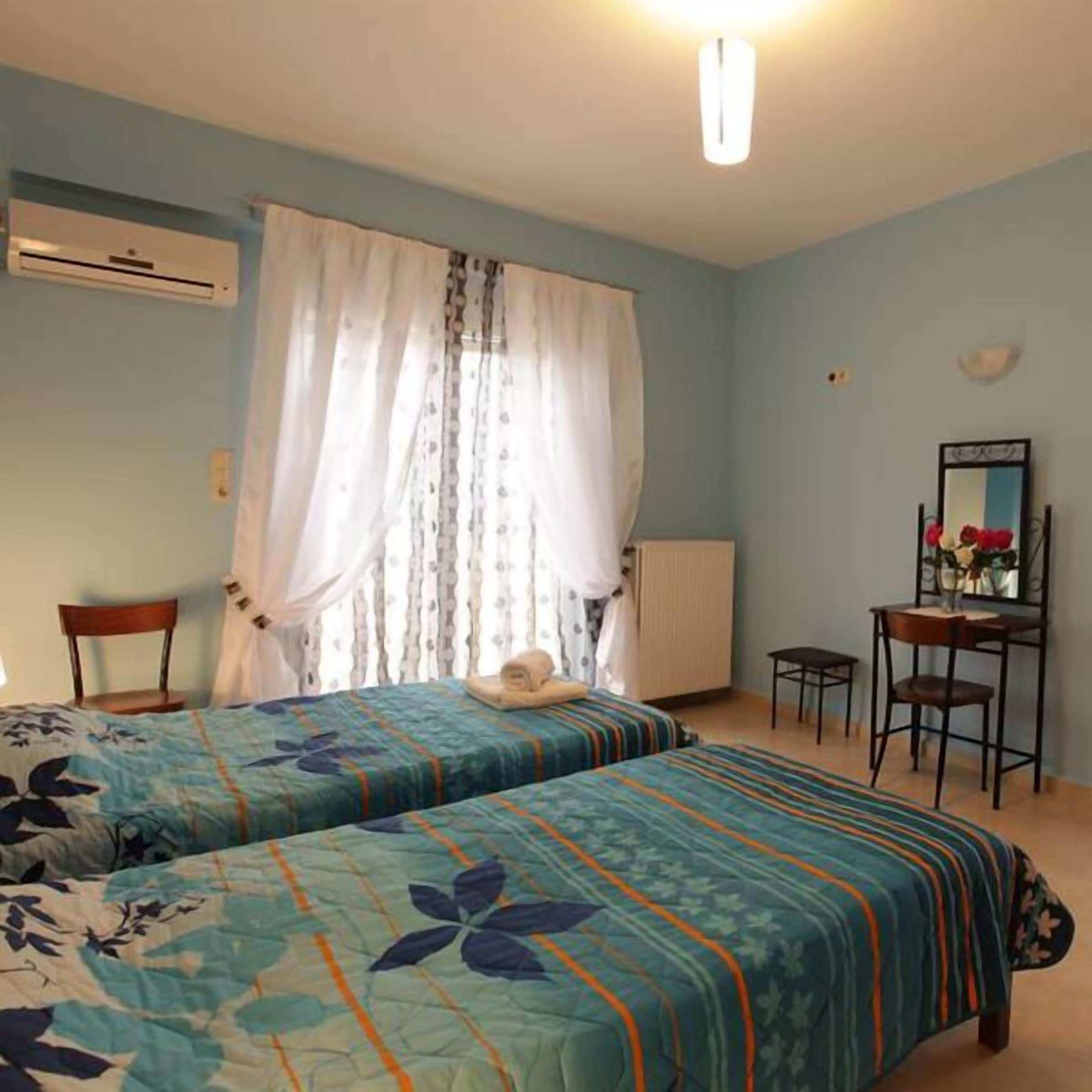 A bedroom with two beds, a chair, a desk, and a mirror.