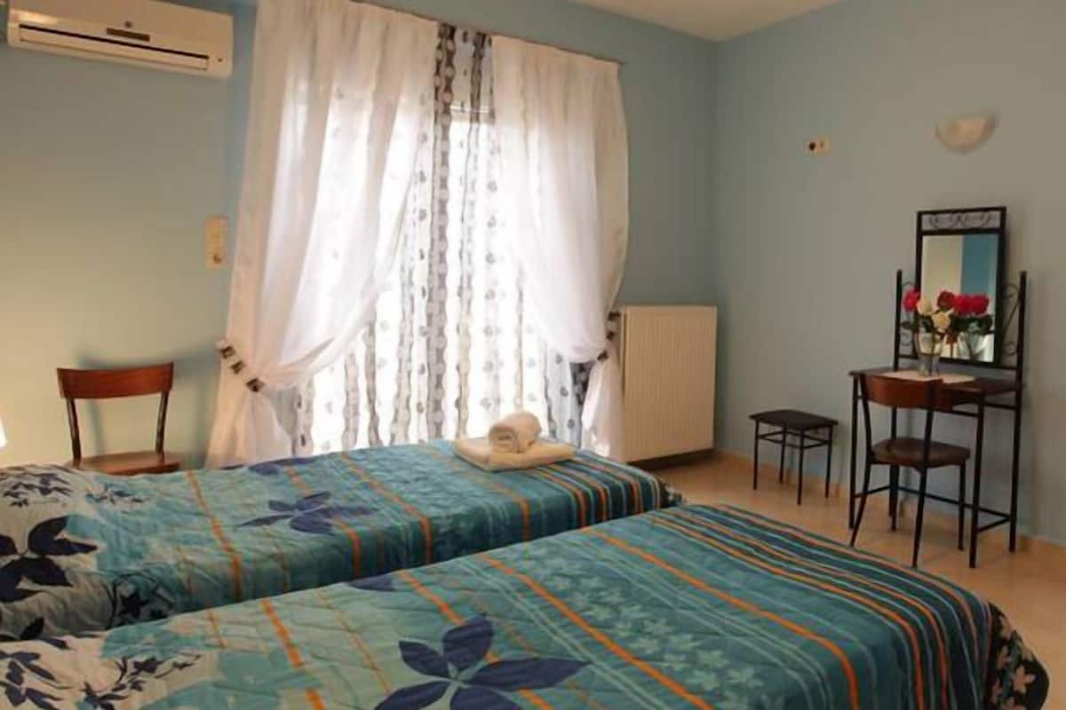 A bedroom with two beds, a chair, a desk, and a mirror.