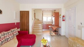Una sala de estar con un sofá rojo, un comedor con mesa y sillas, y una cocina al fondo.