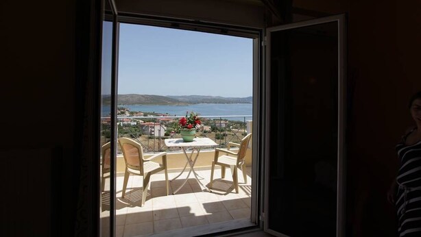 Un balcón con una mesa y sillas, con vistas a un paisaje marino y montañoso.